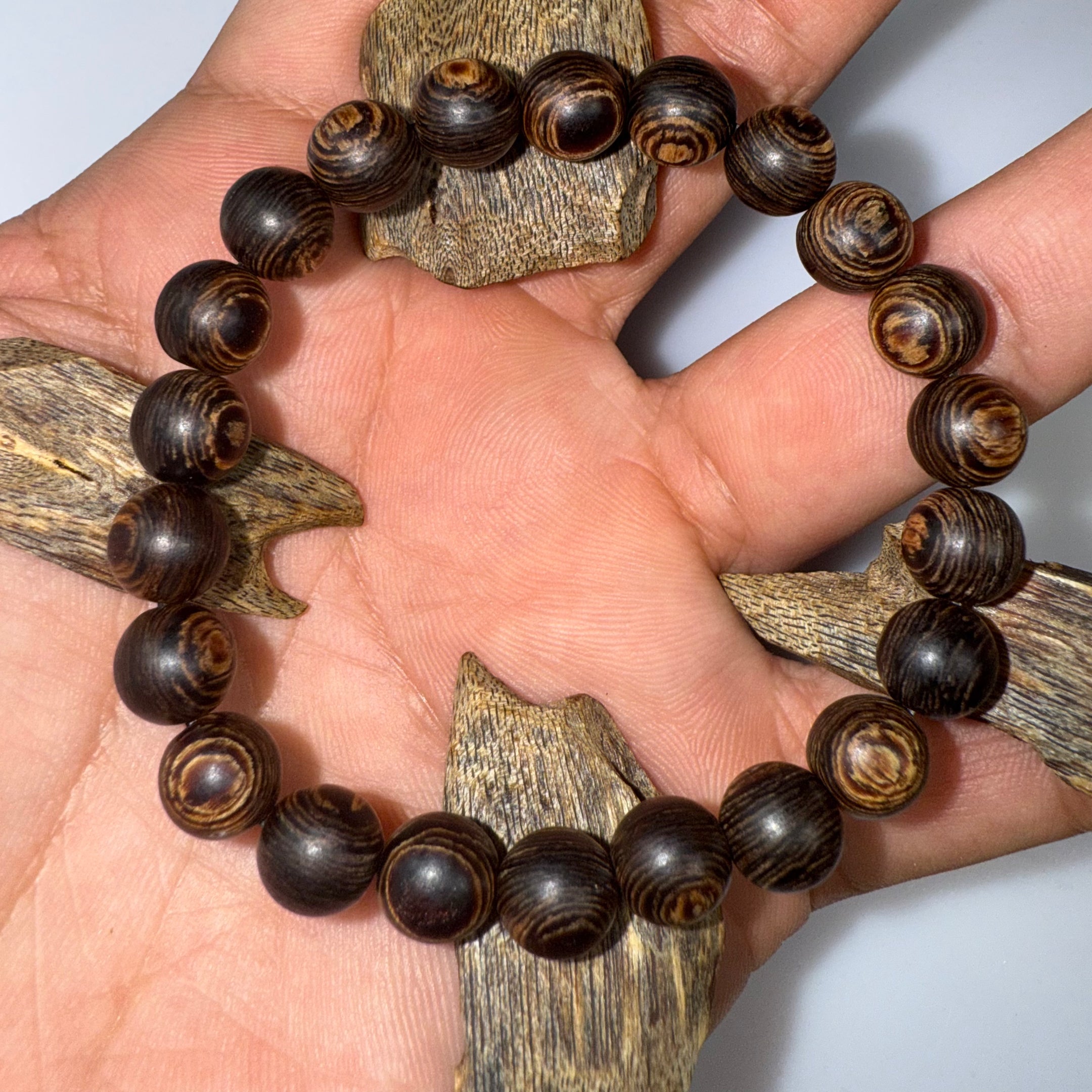 Authentic agarwood bracelet online held in a hand above pieces of raw agarwood
