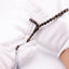 Buy agarwood prayer beads with a grey tassel held between white-gloved hands