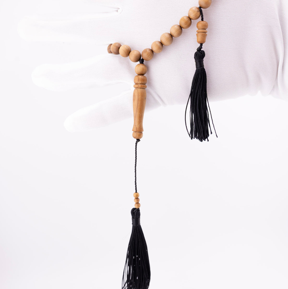 Sandalwood prayer strand for sale held in a white-gloved hand with black tassels visible