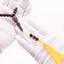 Buy agarwood prayer beads with a carved centerpiece and yellow tassel held in white-gloved hands