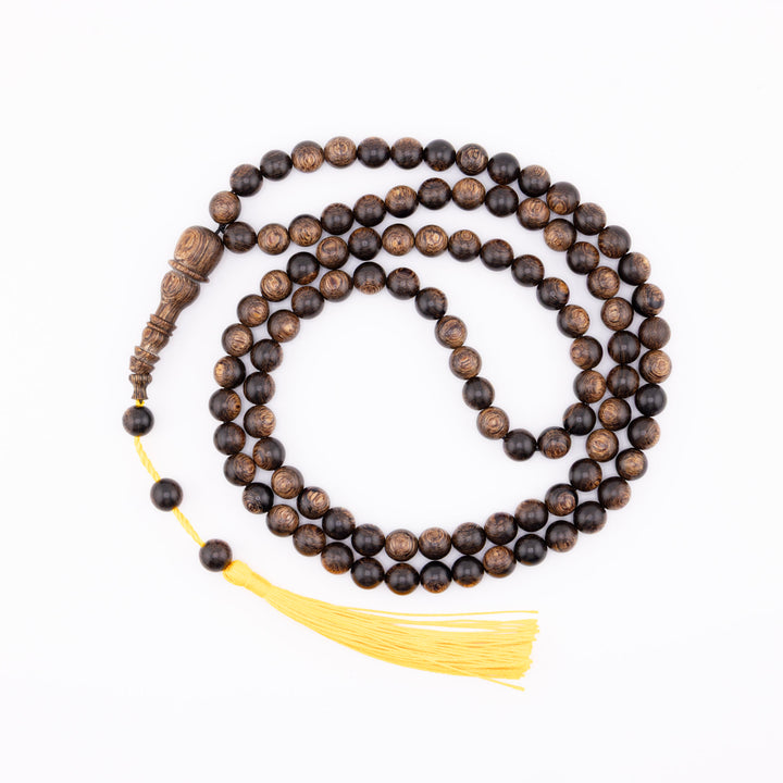 Long agarwood prayer beads coiled on a white background with a yellow tassel