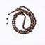 Long agarwood prayer beads coiled on a white background with a white tassel