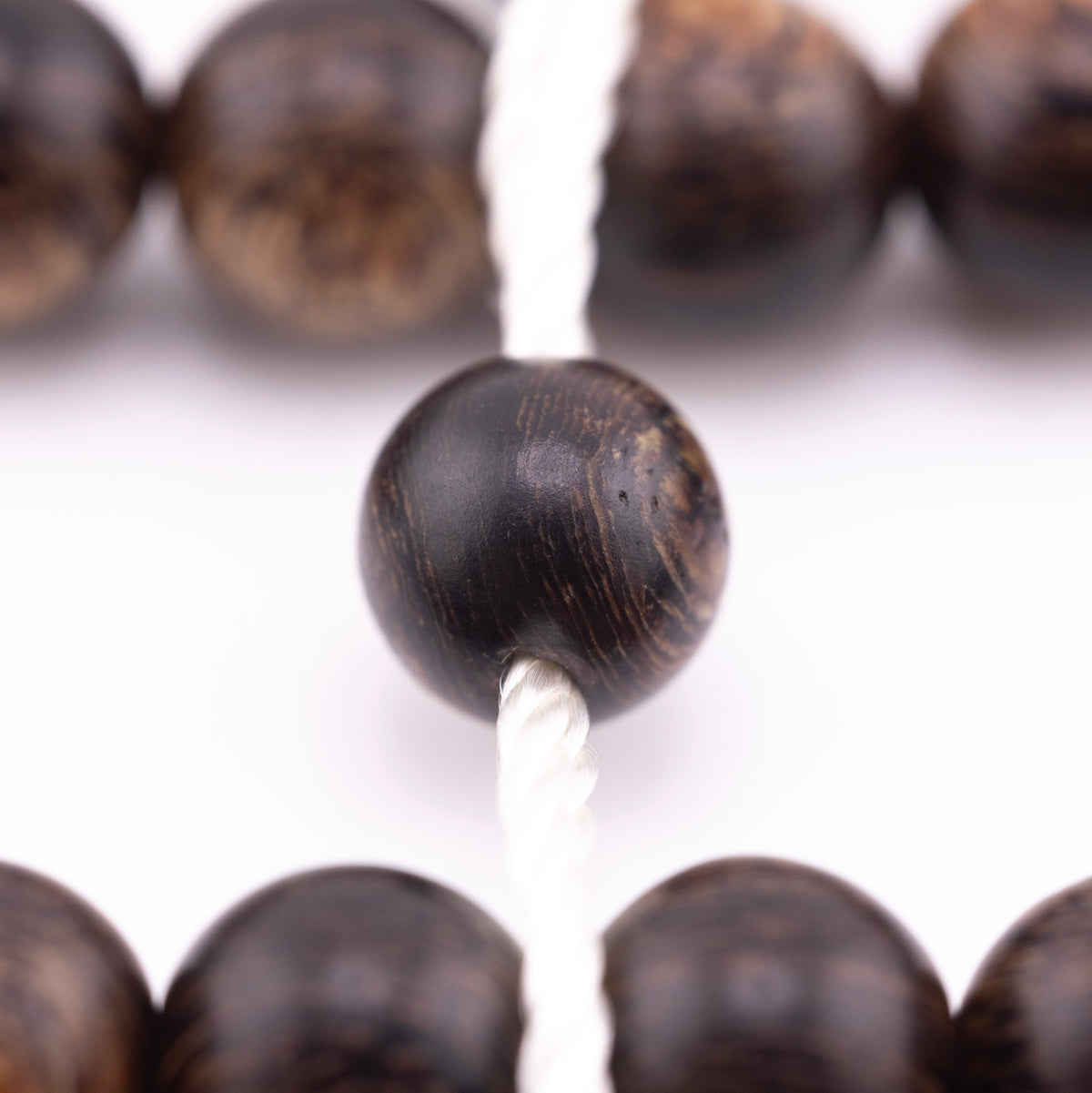 Long agarwood prayer beads in a macro view of one bead threaded onto white cord