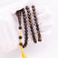 Long agarwood prayer beads with yellow cord and tassel held in a white-gloved hand