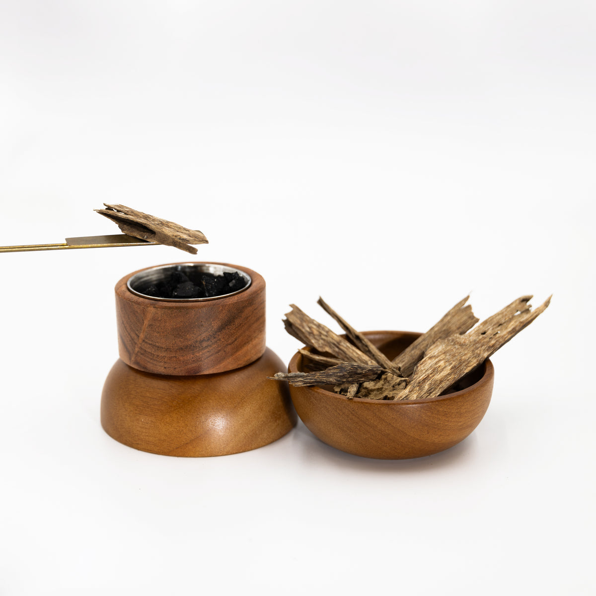 Natural agarwood chips beside a wooden incense heater and metal tongs